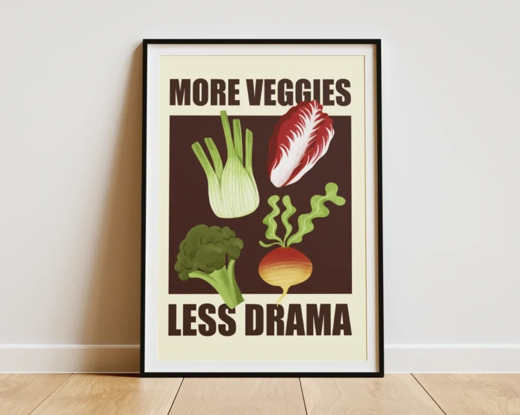 Poster incorniciato in legno nero appoggiato a terra che mostra un'illustrazione grafica di un finocchio, un radicchio rosso, un broccolo e una barbabietola su sfondo scuro e testo “more veggies, less drama” per Green Carrots