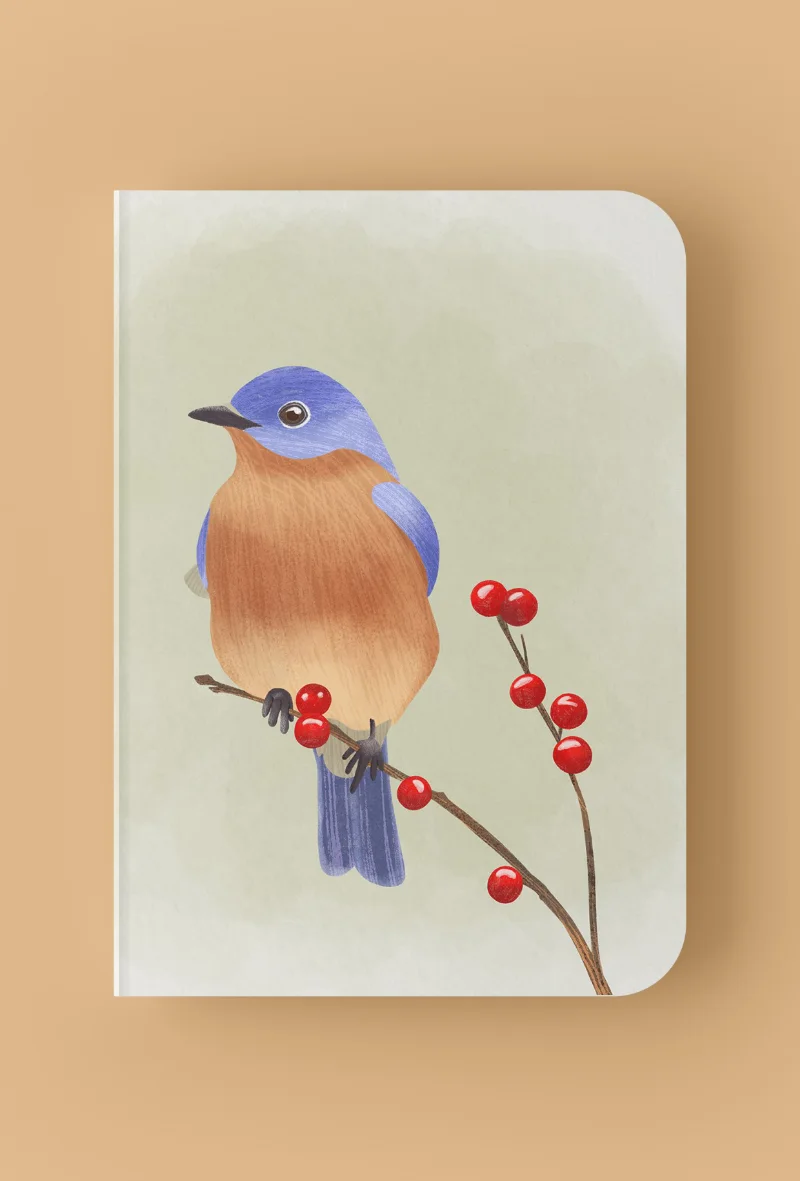 Mockup di agenda con copertina illustrata, raffigurante un uccellino blu e arancione appoggiato su un ramo con le bacche rosse, parte della collezione Ripostiglio Creativo