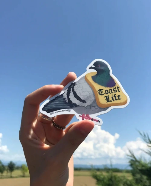 Sticker illustrato reale di un piccione con al collo una collana di fetta di pane e la scritta "toast life"