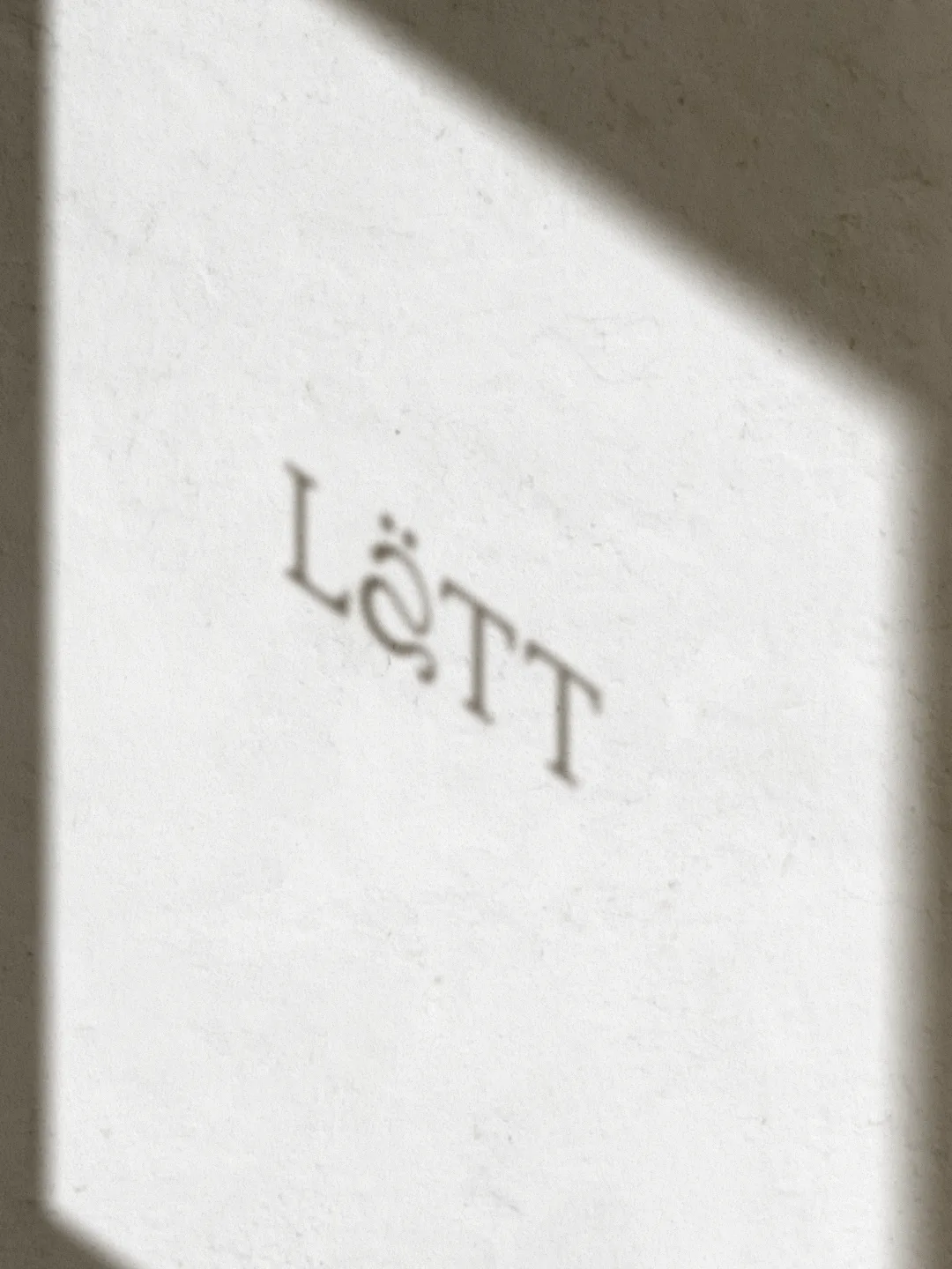 L'ombra elegante della vetrofania con il logo Lätt proiettata su una superficie chiara e materica.