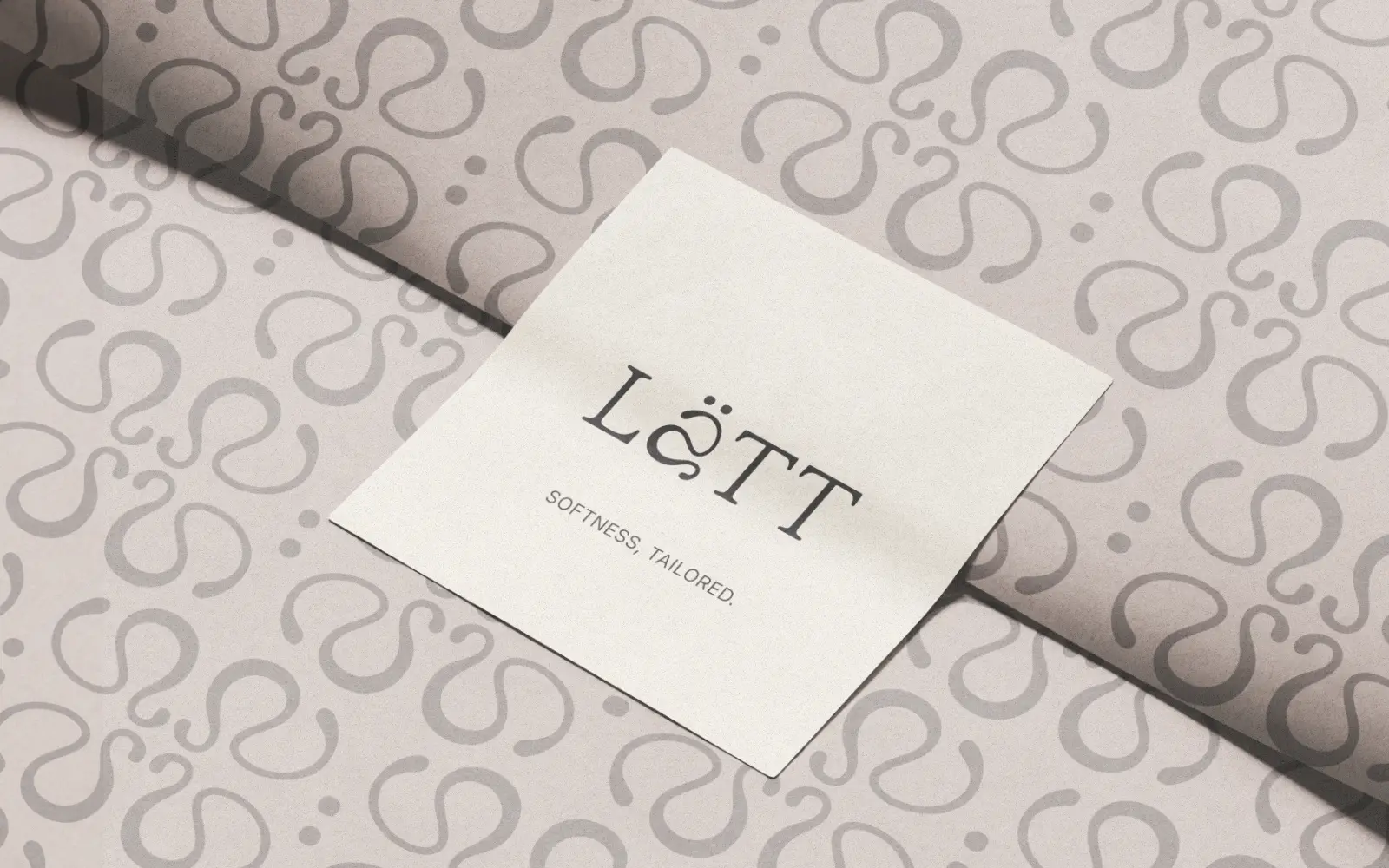 Dettaglio dell'etichetta Lätt, con logo e motto, posizionata sopra una carta decorata con il motivo ripetuto a riccioli del brand